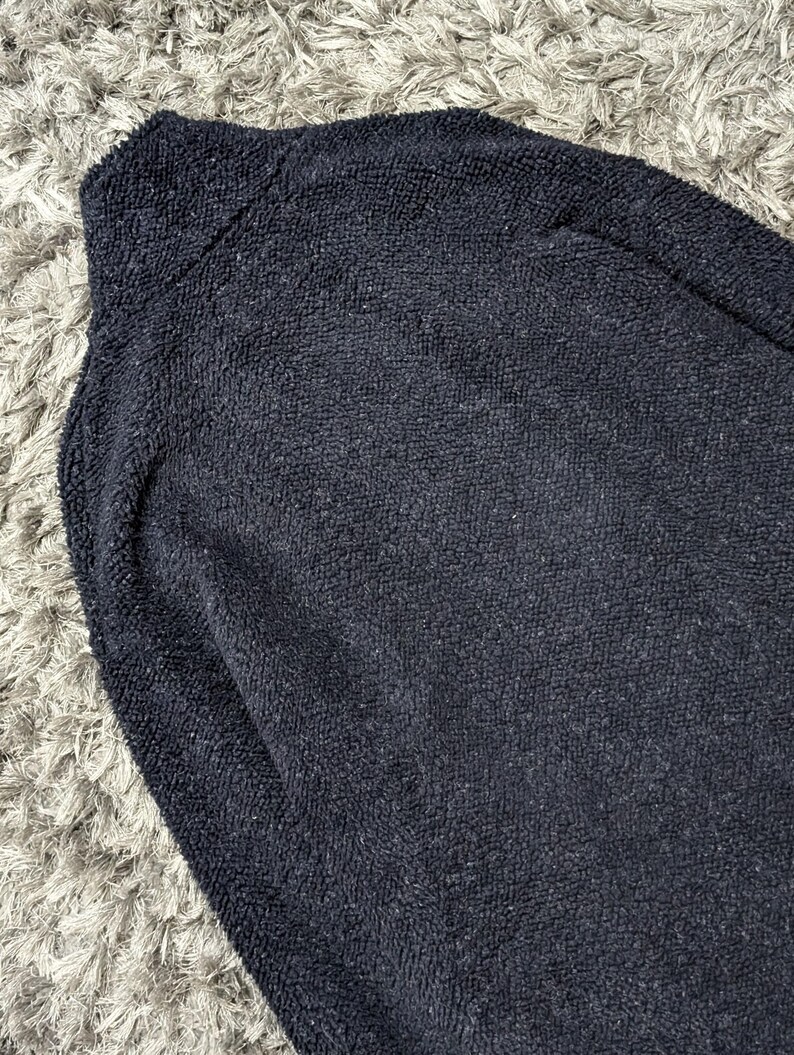 May include: A navy blue fleece jacket with a high collar. The jacket has a soft, textured appearance. The image is a close-up of the jacket, showing the details of the fabric.