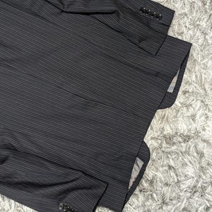May include: A dark gray pinstripe blazer with four buttons on each sleeve. The blazer is made of a textured fabric and has a classic design. The interior lining is visible in the image.