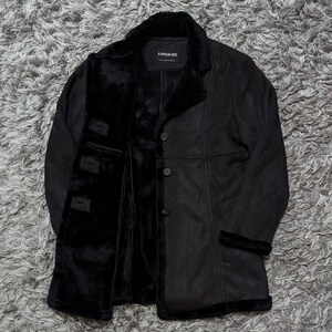 May include: A black coat with a soft black faux fur lining and trim. The coat features a notched collar, long sleeves with fur cuffs, and a front button closure. A label inside the neck reads KANSAI BIS. The exterior has a smooth, matte finish.