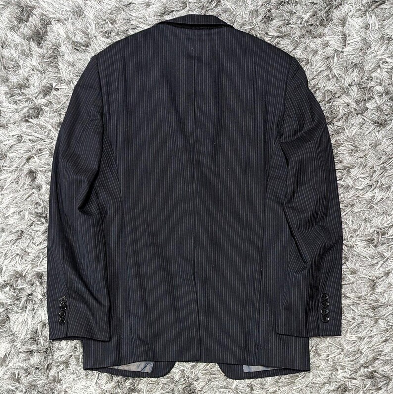 May include: A navy blue pinstripe blazer with a classic design. The blazer features a notched lapel, three-button closure on the sleeves, and a two-button front. The fabric has a subtle vertical stripe pattern.