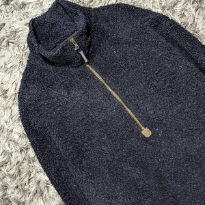 May include: A navy blue fleece pullover with a high collar and a gold-colored zipper. The textured fabric is visible in this close-up shot of the top. The zipper extends down the front of the garment.