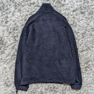 May include: A navy blue fleece jacket with a high collar and a drawstring at the hem. The jacket has long sleeves and a soft, textured appearance. The jacket is displayed on a gray, textured surface.