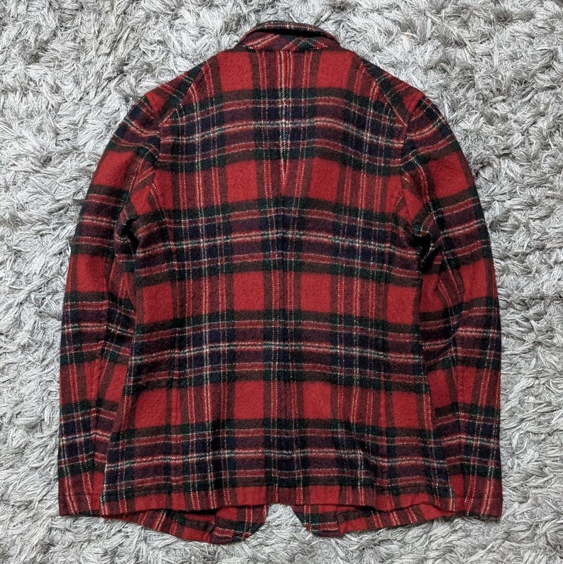 May include: A red and black plaid blazer. The jacket has a classic plaid pattern with a mix of red, black, and green. The blazer has a notched collar and two front pockets. The fabric appears to be a wool blend.