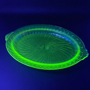 May include: A bright green, oval-shaped glass serving dish with a swirl pattern. The dish has a raised rim and a scalloped edge.