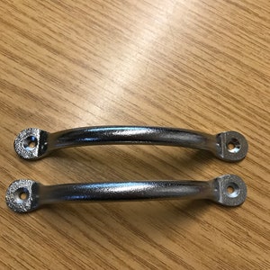 May include: Two silver metal cabinet door handles with rounded edges and a smooth finish. The handles are on a wooden surface.