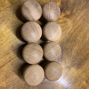 May include: Eight unfinished wooden knobs with a rounded shape and a natural wood grain pattern. The knobs are arranged in two columns of four on a wooden surface.