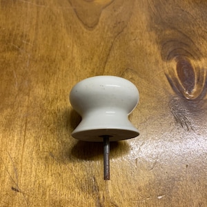 May include: White ceramic cabinet knob with a screw. The knob has a rounded top and a flat base.