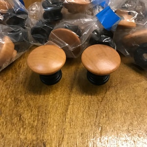 May include: Two wooden knobs with black bases. The knobs are round and have a light brown finish. The knobs are packaged in clear plastic bags.