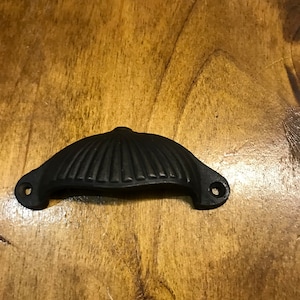May include: Black cast iron drawer pull with a scalloped design. The pull has two holes for mounting.