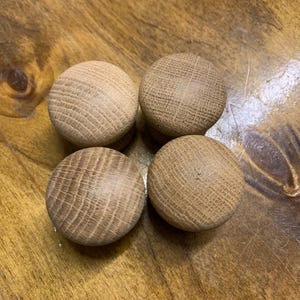 May include: Four light brown wooden knobs with a textured, cross-grain pattern. The knobs are circular and sit on a wooden surface, highlighting the natural wood grain.