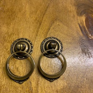 May include: Two antique brass cabinet door pulls with ornate details and a ring handle.