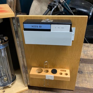May include: Wooden box with a light finish, containing a black box with the text "IB 5224" and a metal tray. A small wooden shelf holds tools and a safety pin. The box is open, revealing its contents.