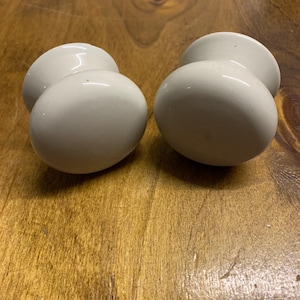 May include: Two white ceramic cabinet knobs with a rounded top and a slightly raised base.