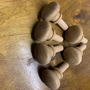 May include: Six wooden knobs with a round top and a threaded stem. The knobs are a light brown colour and have a slightly rough texture.