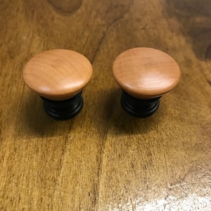 May include: Two wooden knobs with black bases. The knobs are round and have a smooth, light brown finish.