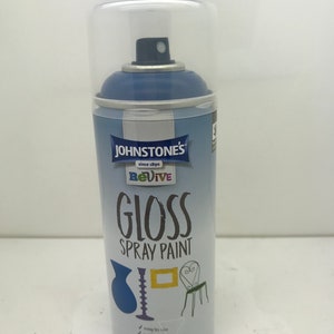 May include: A blue can of Johnstone's Revive Gloss Spray Paint. The can has a white label with the brand name, product name, and instructions for use. The can is sitting on a white surface.