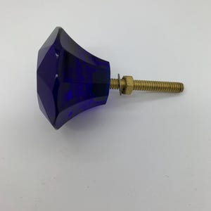 May include: A faceted, deep blue glass cabinet knob with a brass screw and nut. The knob has a geometric design and is suitable for furniture restoration or adding a decorative touch to cabinets and drawers.