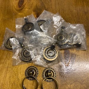 May include: A set of ten antique gold cabinet knobs with a ring pull. The knobs have a decorative, ornate design.