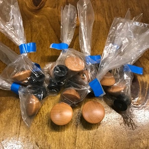 May include: A close-up of a group of wooden knobs in plastic bags. The knobs are round and have a natural wood finish. They are arranged on a wooden surface.