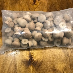 May include: A plastic bag filled with a large quantity of unfinished wooden knobs. The knobs are round with a small, raised centre. They are a light brown colour.