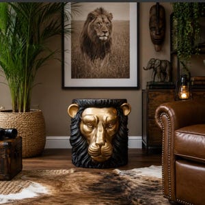 May include: A cylindrical side table featuring a sculpted lion head design. The lion's face is finished in a metallic gold tone, while the surrounding mane and the base of the table are rendered in a solid matte black colour, creating a bold contrast.