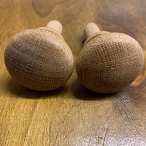 May include: Two wooden knobs with a round, textured top and a threaded stem. The knobs are a light brown colour.