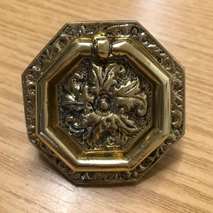 May include: A gold octagonal door pull with a decorative floral design and a ring handle.