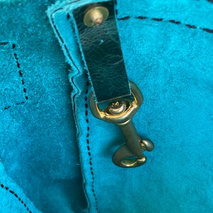 May include: Close-up of a teal blue leather bag with a black leather strap and a gold metal clasp.