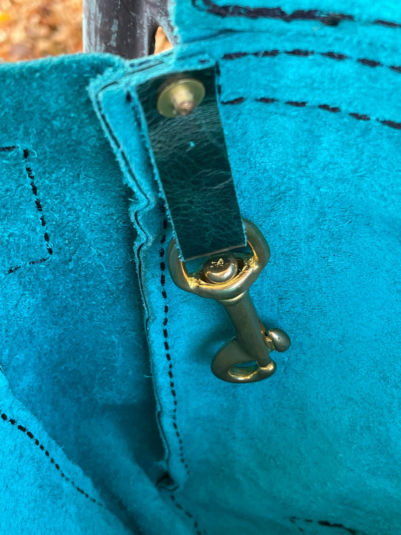 May include: Close-up of a teal blue leather bag with a black leather strap and a gold metal clasp.