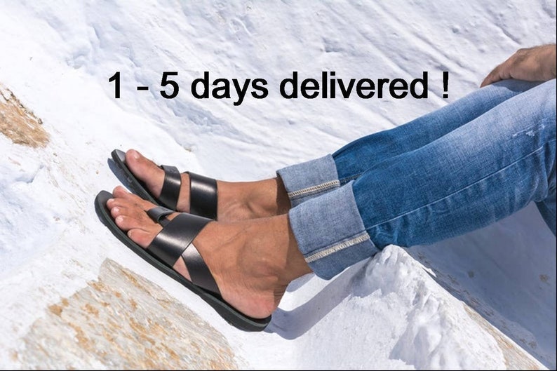 K&ouml;nnte beinhalten: Schwarze Ledersandalen mit einem Kreuzriemen-Design. Die Sandalen werden mit einer blauen Jeans getragen. Der Text "1 - 5 days delivered !" ist im Bild zu sehen.