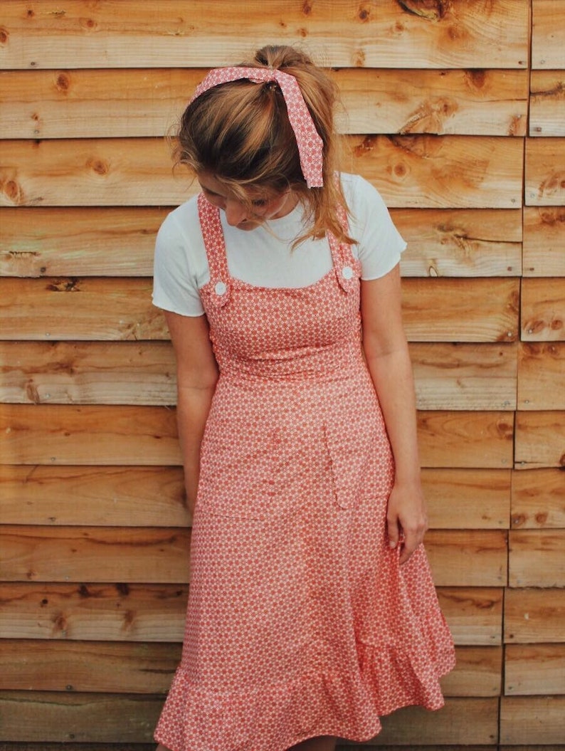 The ROBYN Pinafore Handmade pinafore dress in red floral fabric with cross back straps ruffle hem and pockets