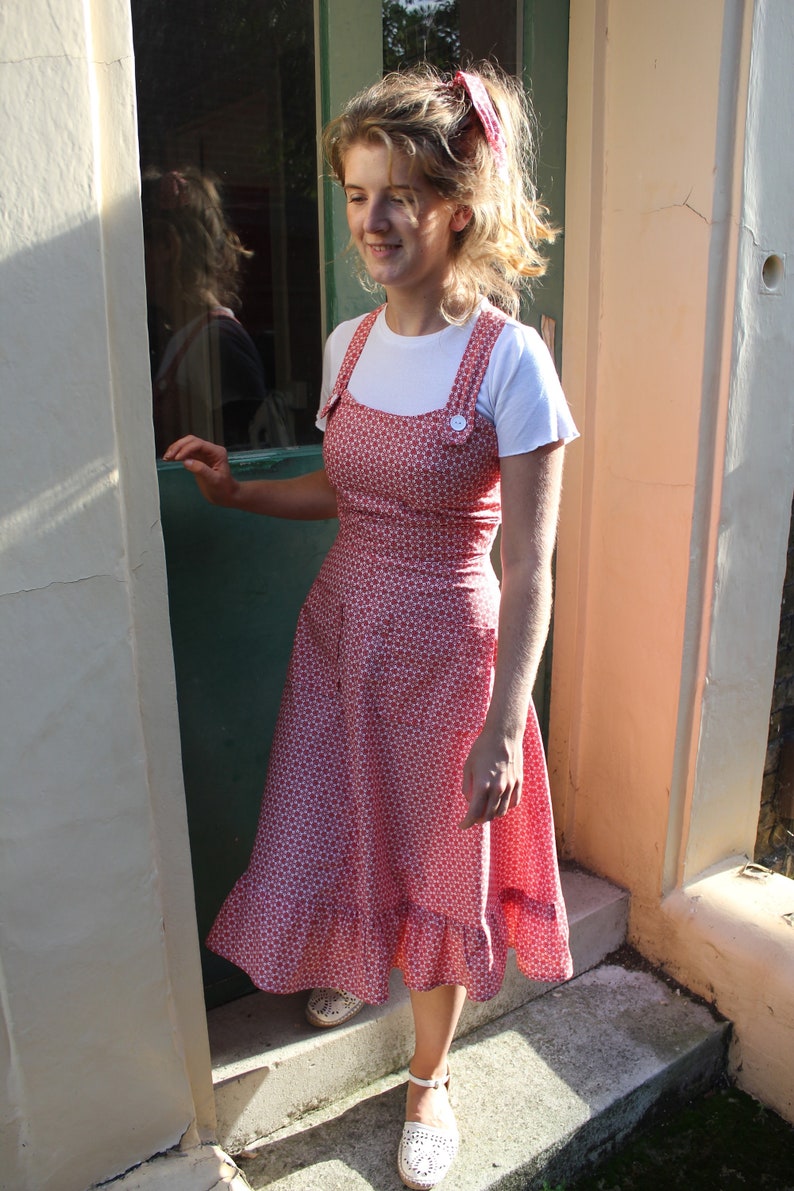 The ROBYN Pinafore Handmade pinafore dress in red floral fabric with cross back straps ruffle hem and pockets
