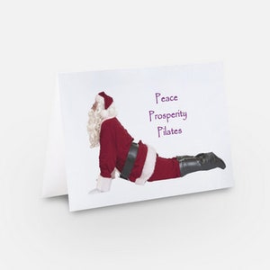 Pode incluir: Um Papai Noel vestido com um terno vermelho e um cinto preto está fazendo uma pose de yoga, com o texto "Peace Prosperity Pilates" escrito em roxo acima dele.
