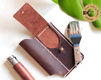 May include: A dark brown leather pouch with white stitching and a metal snap closure, featuring an open flap. Beside the pouch lies a wooden-handled folding knife and a stainless steel spork with the text N°08 engraved on the handle.