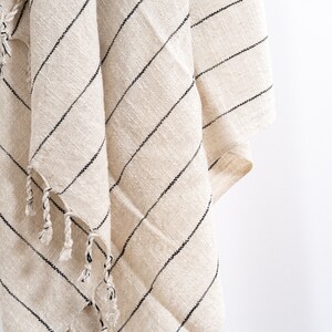 May include: A white and black striped throw blanket with fringe tassels. The blanket is made of a soft, woven fabric.