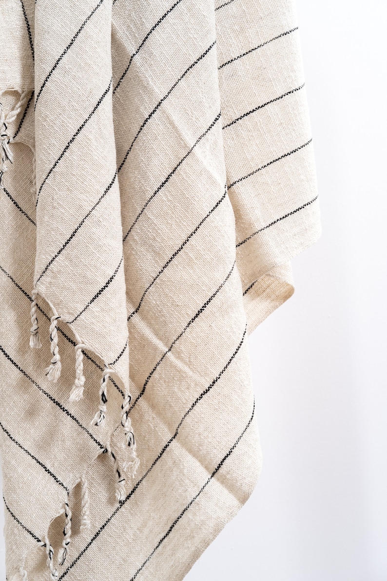 May include: A white and black striped throw blanket with fringe tassels. The blanket is made of a soft, woven fabric.