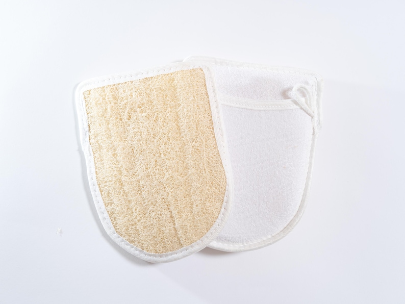 Op de afbeelding: Een paar scrubhandschoenen voor in bad, een van natuurlijke loofah en de andere van zacht wit materiaal.