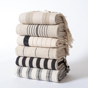 May include: A stack of six striped towels in black and white with fringe edges. The towels are folded and stacked on a white surface.