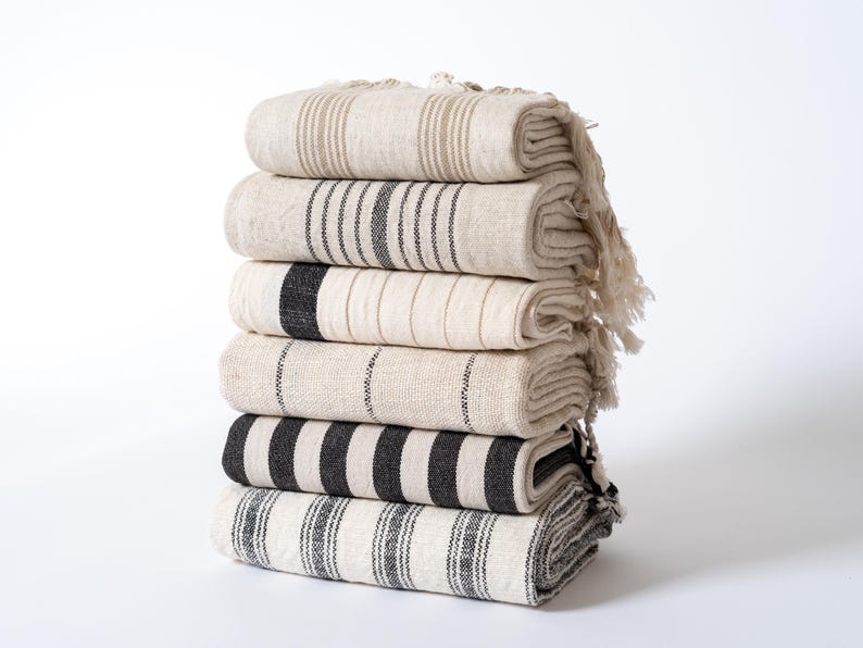Peut inclure: Une pile de six serviettes ray&eacute;es en noir et blanc avec des franges. Les serviettes sont pli&eacute;es et empil&eacute;es sur une surface blanche.