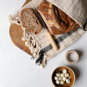 Peut inclure: Une miche de pain au levain sur une planche &agrave; d&eacute;couper en bois avec un couteau et un bol de boulettes de mozzarella. Le pain est partiellement tranch&eacute; et le fromage est saupoudr&eacute; d'herbes.