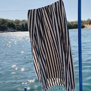May include: A black and white striped beach towel hanging on a blue railing with a view of the ocean in the background.