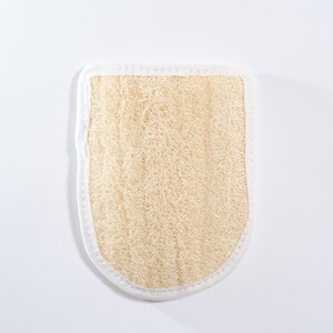 Op de afbeelding: Een beige loofah badspons met een witte rand. De spons is gemaakt van natuurlijke vezels en is ontworpen om de huid te exfoli&euml;ren.