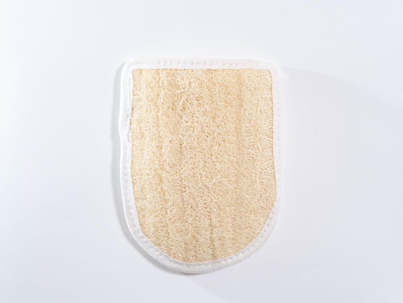 Op de afbeelding: Een beige loofah badspons met een witte rand. De spons is gemaakt van natuurlijke vezels en is ontworpen om de huid te exfoli&euml;ren.