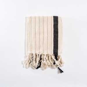 May include: A white hand towel with black stripes and fringe. The towel is made of a soft, absorbent material and is perfect for drying hands or dishes.