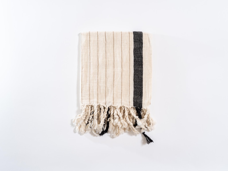 May include: A white hand towel with black stripes and fringe. The towel is made of a soft, absorbent material and is perfect for drying hands or dishes.