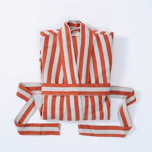 May include: A red and white striped robe with a self-tie belt. The robe is folded in half and laid flat on a white surface.