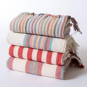 Peut inclure: Une pile de quatre serviettes ray&eacute;es de diff&eacute;rentes couleurs, dont le rouge, le bleu et le blanc. Les serviettes sont pli&eacute;es et dispos&eacute;es soigneusement sur une surface blanche.