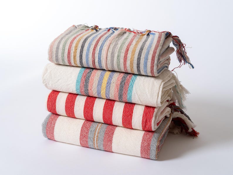 Peut inclure: Une pile de quatre serviettes ray&eacute;es de diff&eacute;rentes couleurs, dont le rouge, le bleu et le blanc. Les serviettes sont pli&eacute;es et dispos&eacute;es soigneusement sur une surface blanche.
