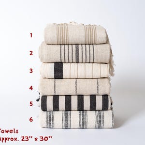 Peut inclure: Six serviettes de toilette empil&eacute;es les unes sur les autres. Les serviettes sont blanches avec des rayures noires. Les serviettes mesurent environ 58 cm sur 76 cm.