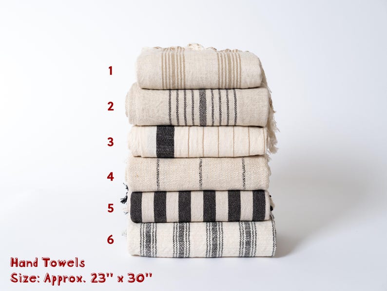 Peut inclure: Six serviettes de toilette empil&eacute;es les unes sur les autres. Les serviettes sont blanches avec des rayures noires. Les serviettes mesurent environ 58 cm sur 76 cm.